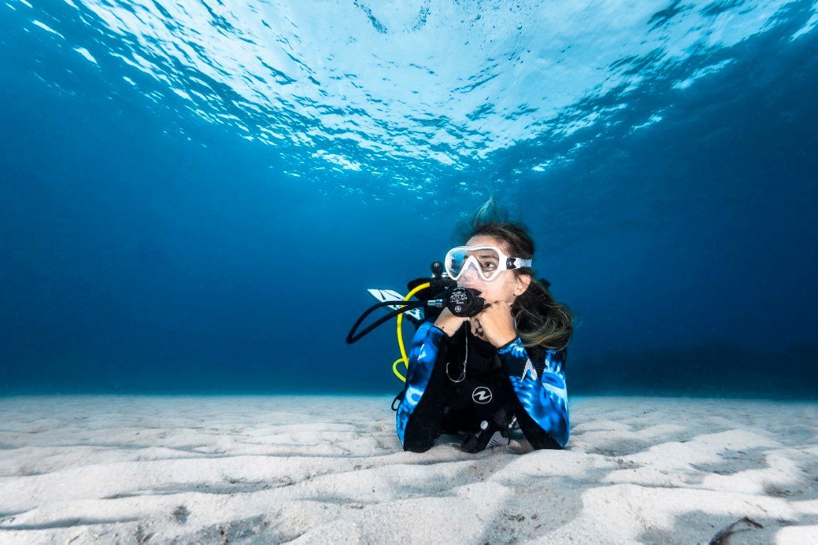 A diver kneeling on white sand below the surface